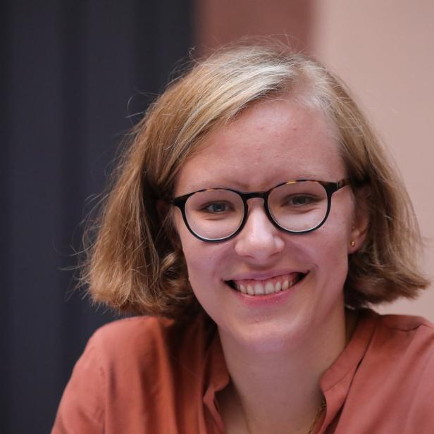 Eine lächelnde junge Frau mit Brille und blonden Haaren.