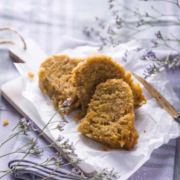 Ein Stück Kuchen liegt auf einem Holzbrett mit lila Blumen dekoriert.