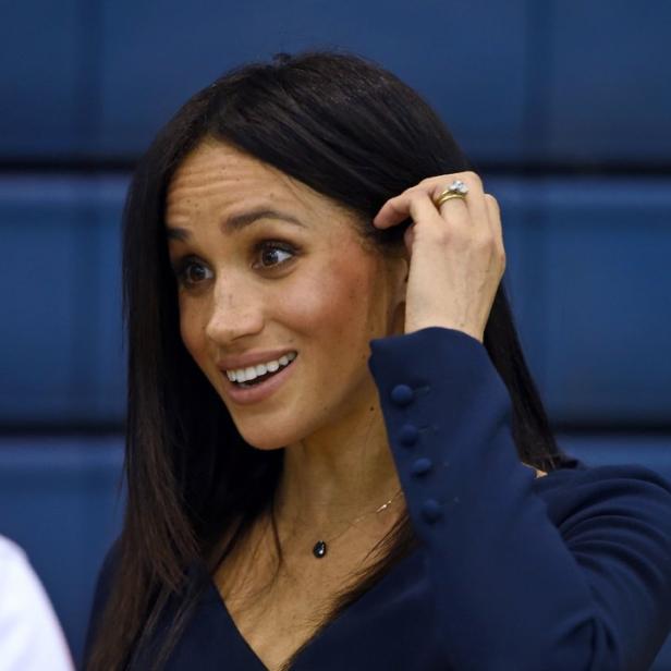 Meghan Markle lächelt und berührt ihr Haar.