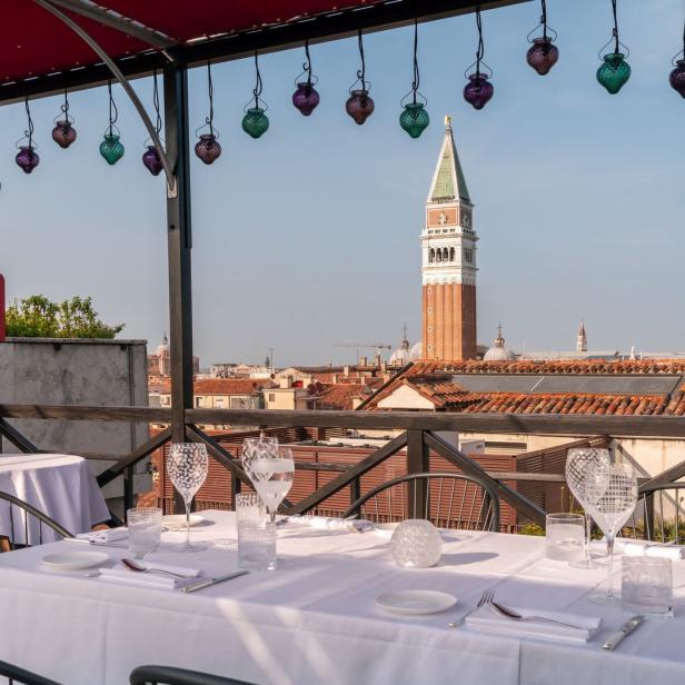 Ein gedeckter Tisch auf einer Dachterrasse mit Blick auf den Campanile in Venedig.