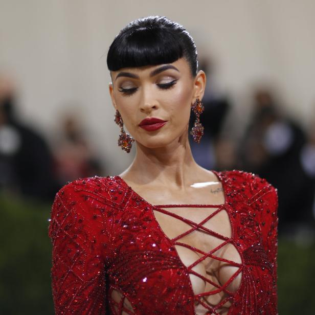 Megan Fox in einem roten, tief ausgeschnittenen Kleid mit passenden Ohrringen.