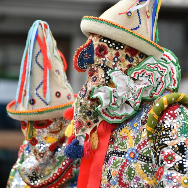 Zwei Personen tragen aufwendige, farbenfrohe Masken und Hüte, vermutlich für eine traditionelle Feierlichkeit.