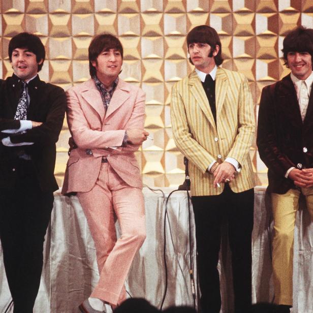 Die Beatles stehen in Anzügen vor einer Wand mit geometrischem Muster.