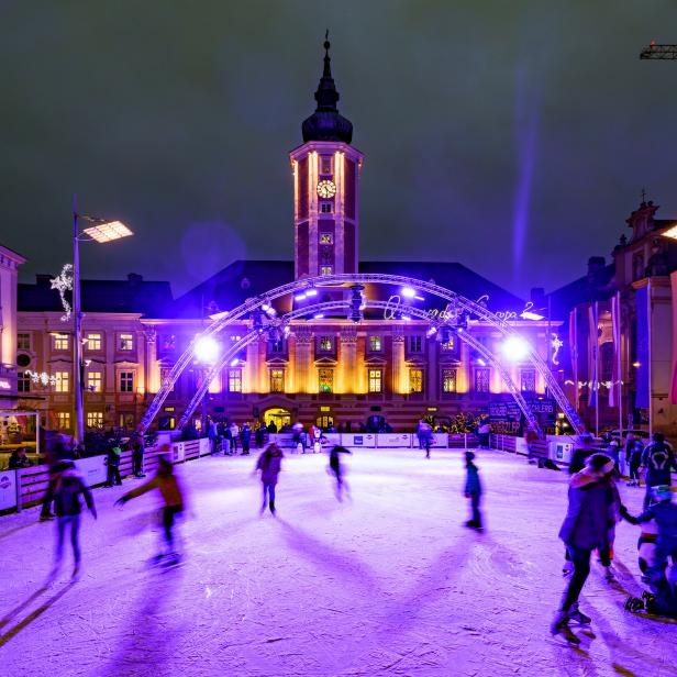 Menschen laufen auf einer Eisbahn vor dem Rathaus in Wels, Österreich.