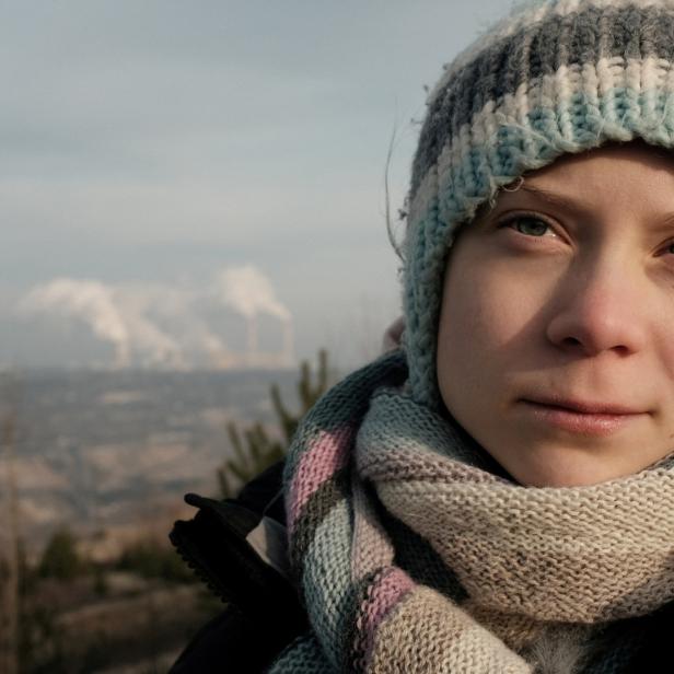Greta Thunberg mit Mütze und Schal vor einer verschmutzten Landschaft.