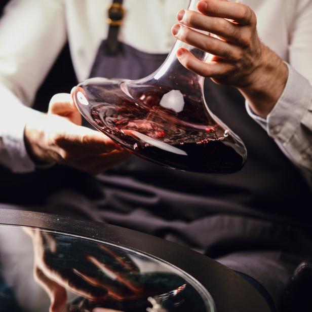 Ein Kellner dekantiert Rotwein in einem eleganten Dekanter.