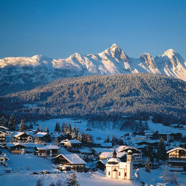 Ein verschneites Dorf in den Alpen mit einer beleuchteten Kirche im Vordergrund.