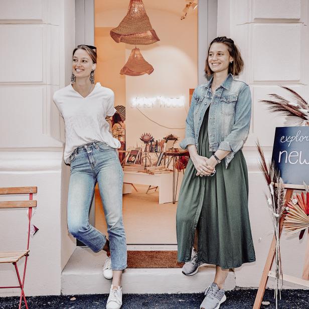 Zwei Frauen posieren vor dem Eingang eines Ladens mit der Aufschrift „Explore the new hood in town“.