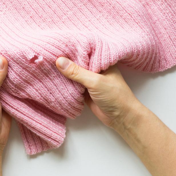 Hände halten einen rosa Strickpullover mit einem Loch.