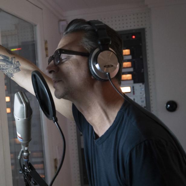 Ein Mann mit Kopfhörern steht vor einem Mikrofon im Aufnahmestudio.