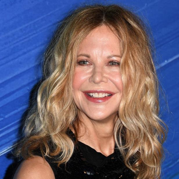 Meg Ryan lächelt vor einem blauen Hintergrund.