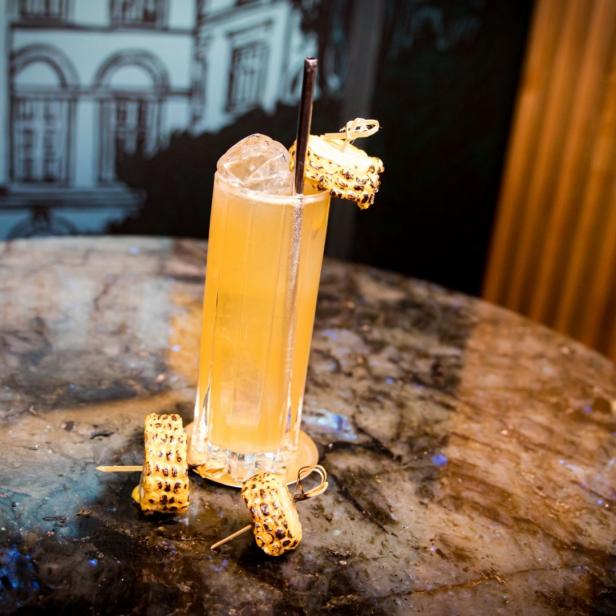 Ein Cocktail in einem hohen Glas, garniert mit gegrilltem Mais.