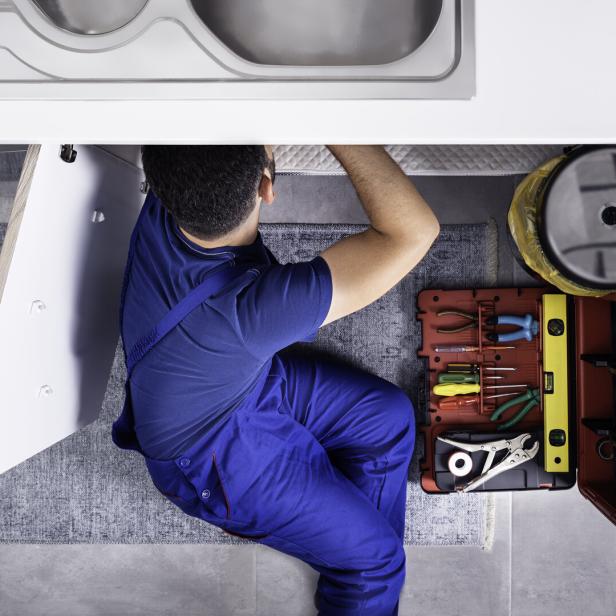 Ein Installateur arbeitet unter einem Waschbecken mit einem offenen Werkzeugkasten neben sich.