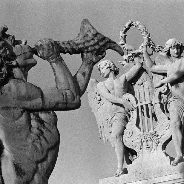 Detailaufnahme von drei Skulpturen mit geflügelten Figuren, von denen eine ein Horn bläst.