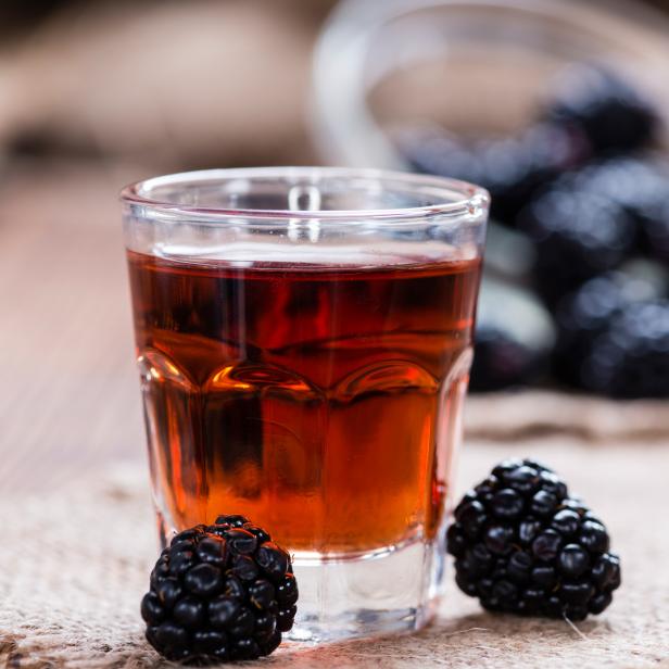 Ein Glas Brombeerlikör steht neben frischen Brombeeren auf einem rustikalen Untergrund.