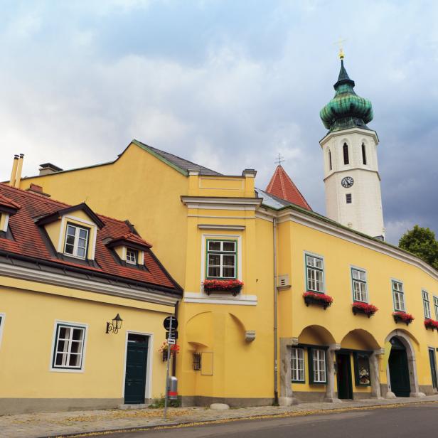 Gelbe Gebäude und ein Kirchturm in Wien-Döbling unter einem bewölkten Himmel.