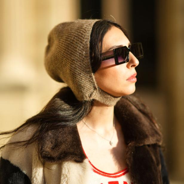 Eine Frau mit Sonnenbrille und Mütze blickt zur Seite.