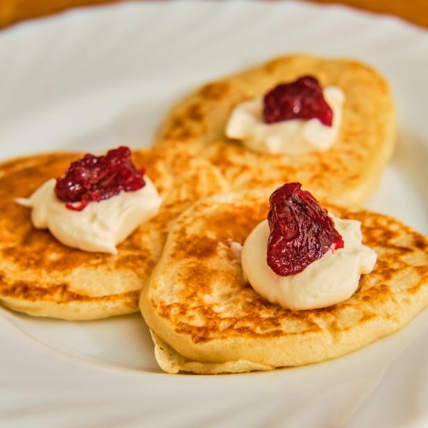 Drei goldbraune Pfannkuchen mit einem Klecks Creme und roter Marmelade auf einem Teller.