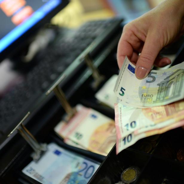 Steuerreform: Eine Hand hält Geldscheine über eine offene Registrierkasse.