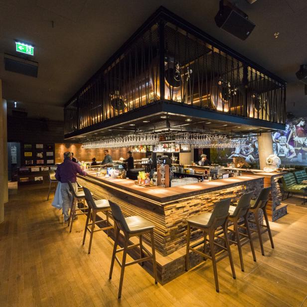 Eine Bar mit Hockern und Gästen in einem modern gestalteten Innenraum.