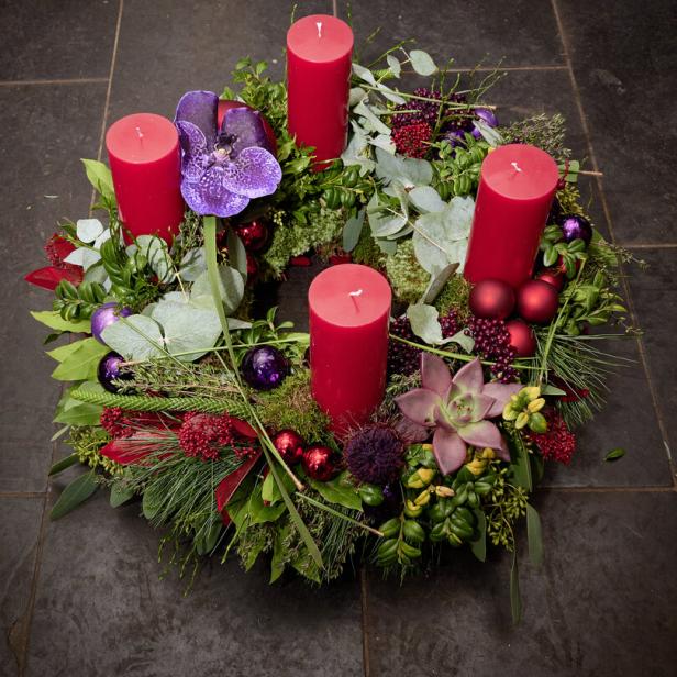 Ein Adventskranz mit vier roten Kerzen, geschmückt mit Blumen und Weihnachtskugeln.