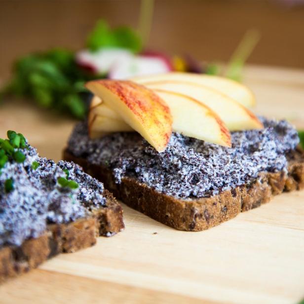 Zwei Brotscheiben mit Mohnaufstrich, eine mit Apfelspalten und die andere mit Schnittlauch belegt.