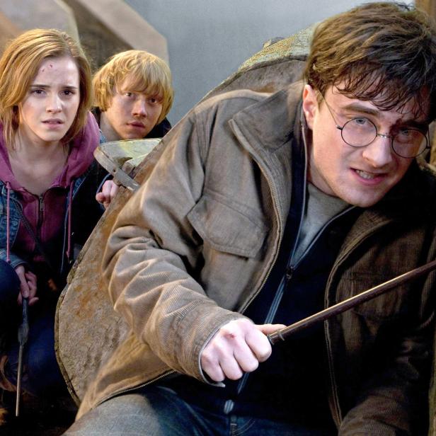 Harry Potter, Hermine Granger und Ron Weasley ducken sich mit gezückten Zauberstäben.