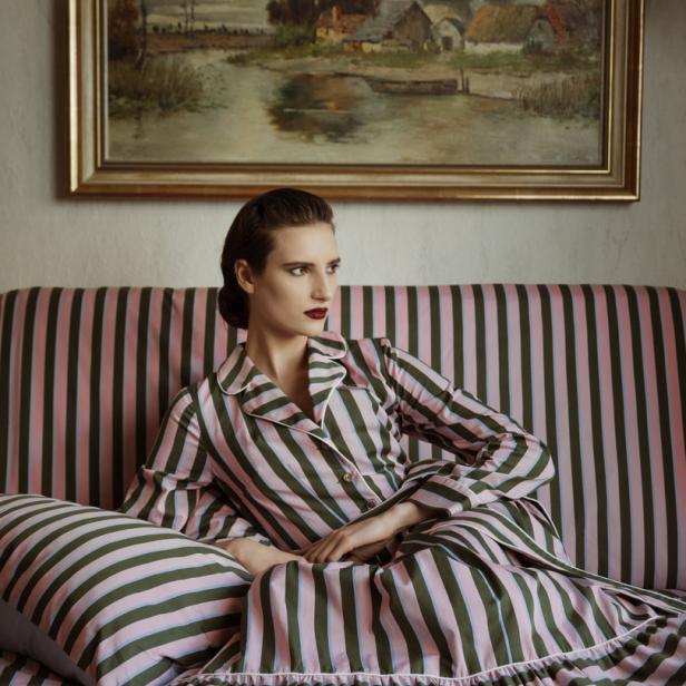 Eine Frau im gestreiften Pyjama sitzt auf einem Sofa vor einem Gemälde.