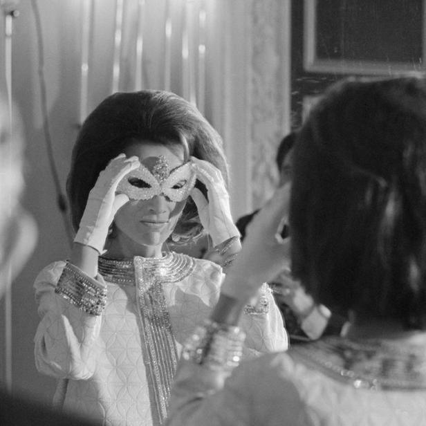Eine Frau mit Handschuhen setzt eine venezianische Maske vor einem Spiegel auf.