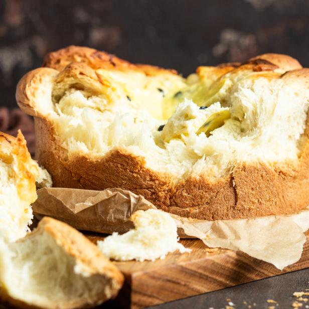 Ein angeschnittener, hoher Kuchen mit gelber Füllung auf einem Holzbrett.
