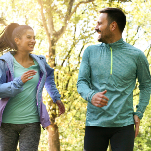 Ein Mann und eine Frau joggen lächelnd durch einen sonnigen Park.