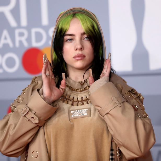 Billie Eilish bei den BRIT Awards 2020 mit grün-schwarzen Haaren und beiger Kleidung.
