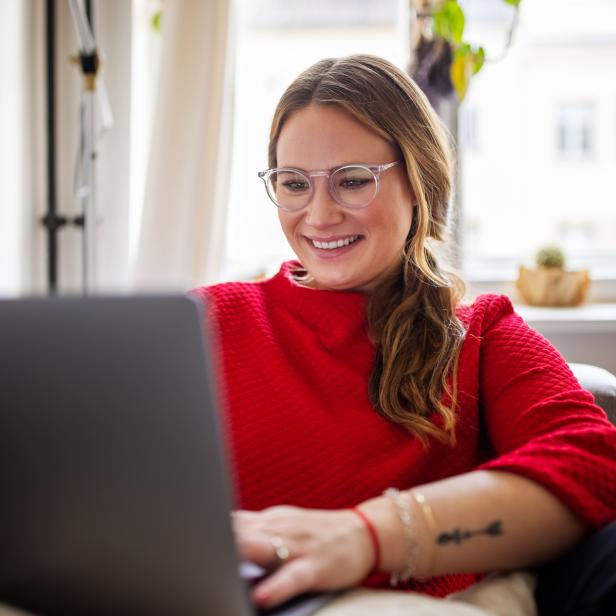 Eine Frau mit Brille lächelt, während sie an einem Laptop arbeitet.