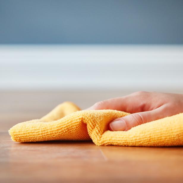 Eine Hand wischt einen Holzboden mit einem gelben Tuch ab.