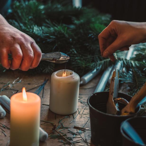 Zwei Personen fertigen einen Adventskranz mit Kerzen und Tannengrün an.