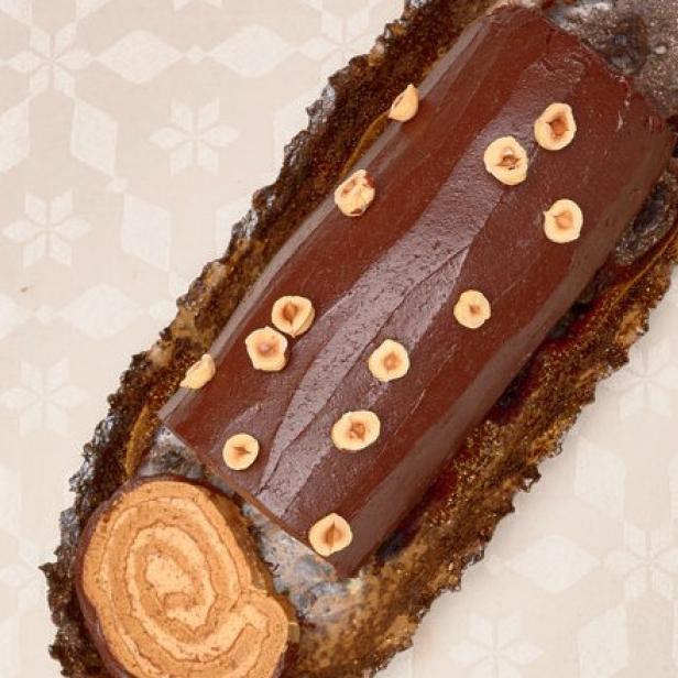 Ein mit Haselnüssen dekorierter Schokoladen-Bûche de Noël auf einer Platte.