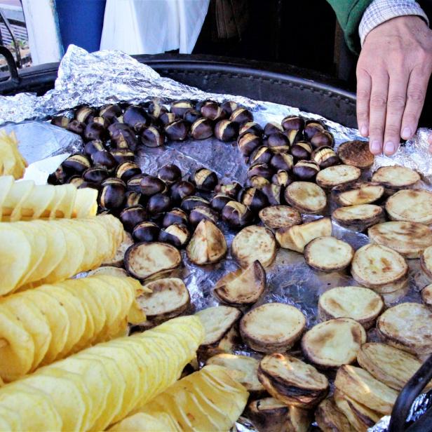 Ein Verkäufer bietet geröstete Kastanien, Kartoffelchips und Bratkartoffeln an.