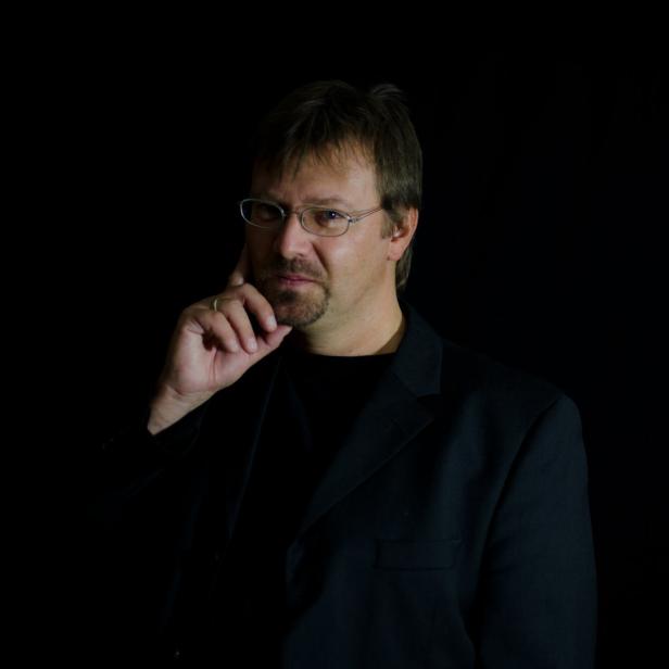 Ein Mann mit Brille und Anzug hält seine Hand ans Kinn.