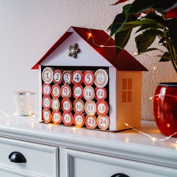 Ein Adventskalender in Form eines Hauses steht auf einer Kommode.