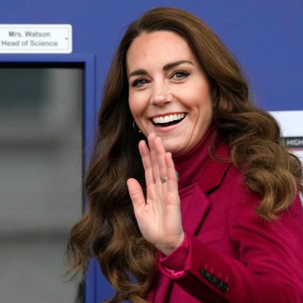 Kate Middleton lächelt und winkt in einem roten Blazer.