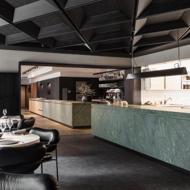 Innenansicht eines eleganten Restaurants mit Tischen und einer Bar aus grünem Marmor.