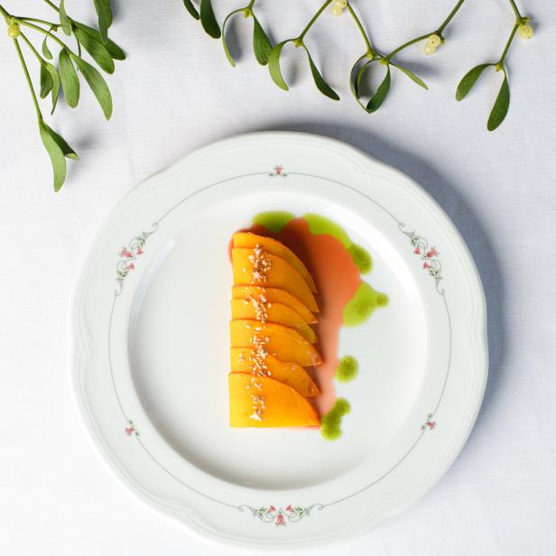 Ein Teller mit geschnittenen Mangos, garniert mit Sesam und grüner Soße, umgeben von Mistelzweigen.