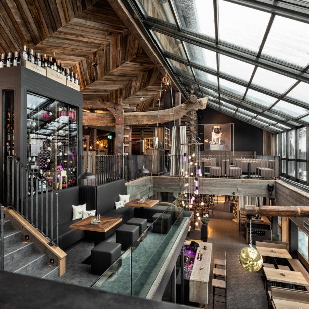 Innenansicht eines Restaurants mit rustikalem Holzdesign und einer großen Fensterfront.