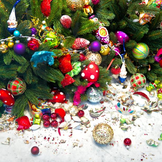 Ein geschmückter Weihnachtsbaum mit vielen bunten Kugeln und zerbrochenem Christbaumschmuck auf dem Boden.