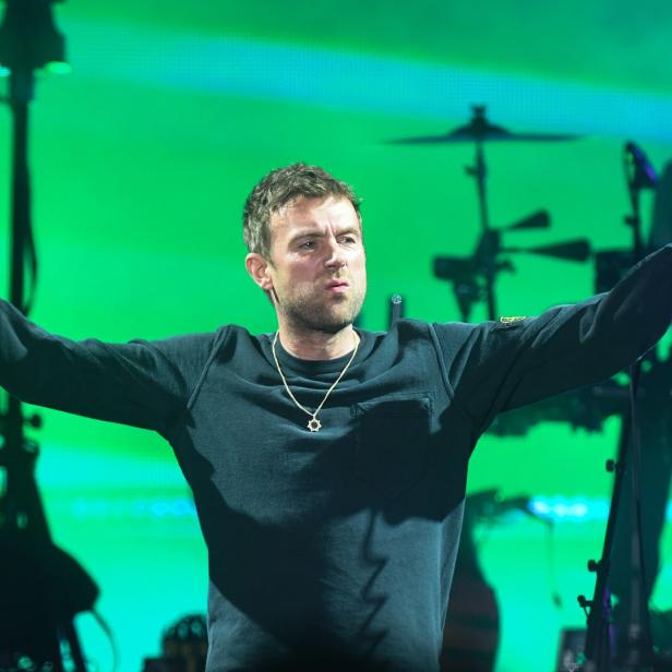 Damon Albarn von Blur tritt mit einem Mikrofon in der Hand auf einer Bühne auf.