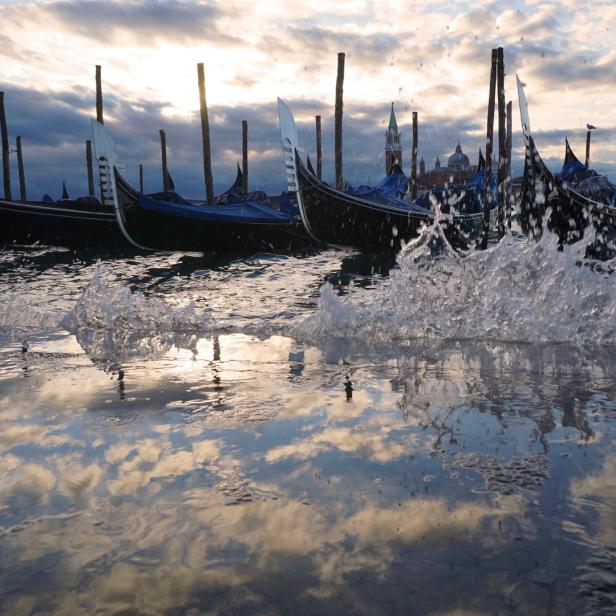 Gondeln liegen im Wasser von Venedig, das den Himmel reflektiert.