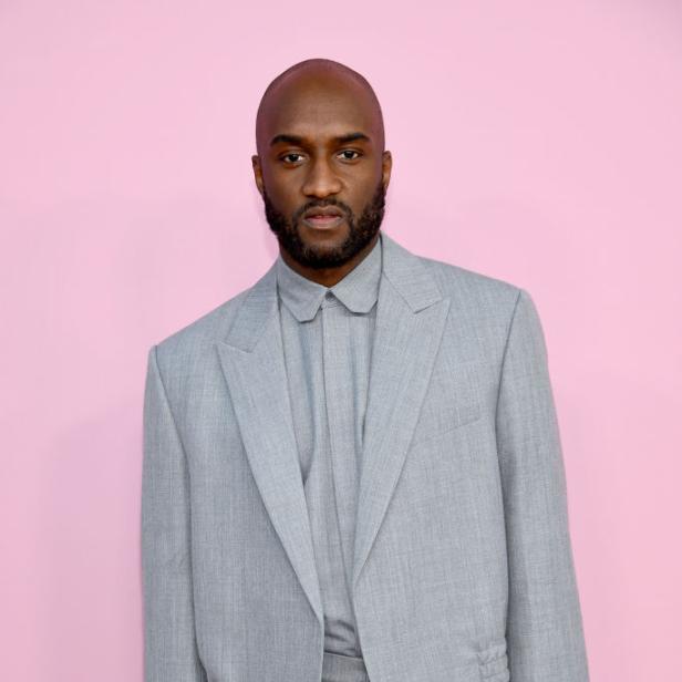 Virgil Abloh trägt einen grauen Anzug vor einem rosa Hintergrund.