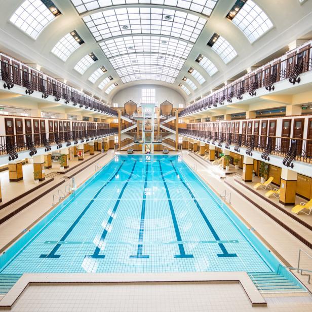 Blick in eine Schwimmhalle mit Schwimmbecken und mehreren Ebenen mit Umkleidekabinen.