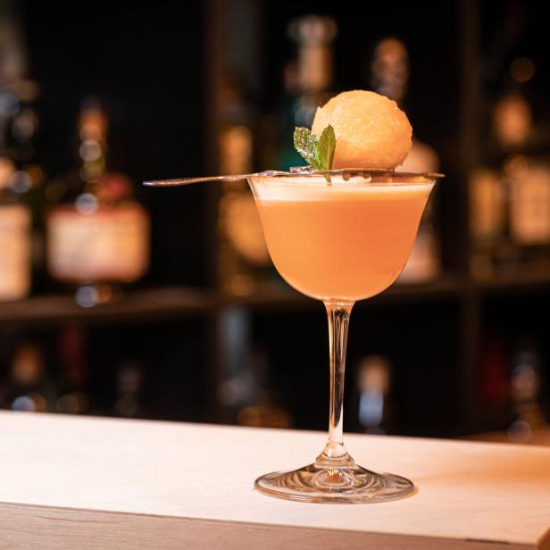 Ein Cocktail in einem eleganten Glas, garniert mit einer Melonenkugel und Minze.