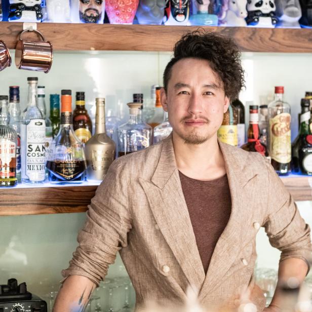 Ein Barkeeper steht vor einem Regal mit verschiedenen Spirituosenflaschen.